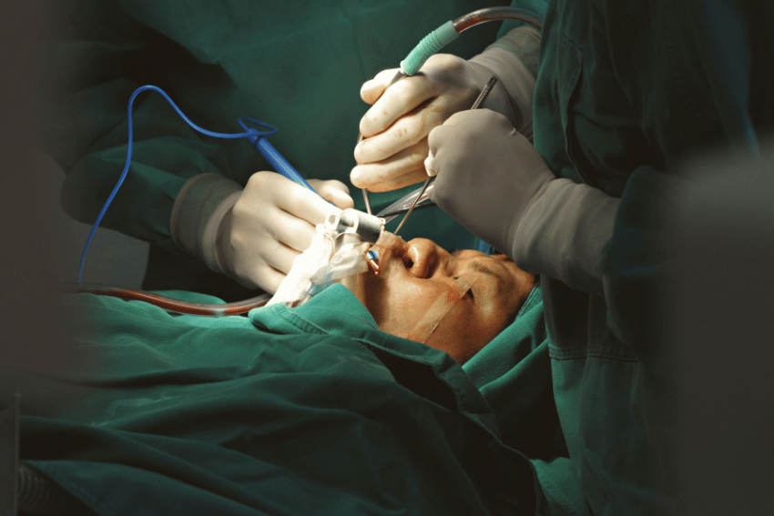 A close-up of a patient undergoing facial surgery after a dog bite, with multiple surgeons in green scrubs and gloves using medical instruments on the patient’s face in an operating room.